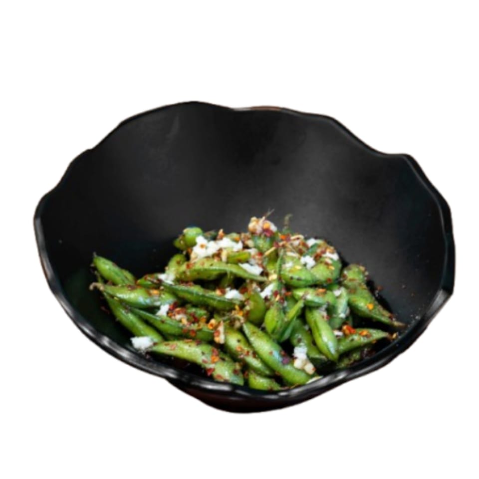 A black bowl filled with green edamame pods, topped with white flakes and red chili pepper.